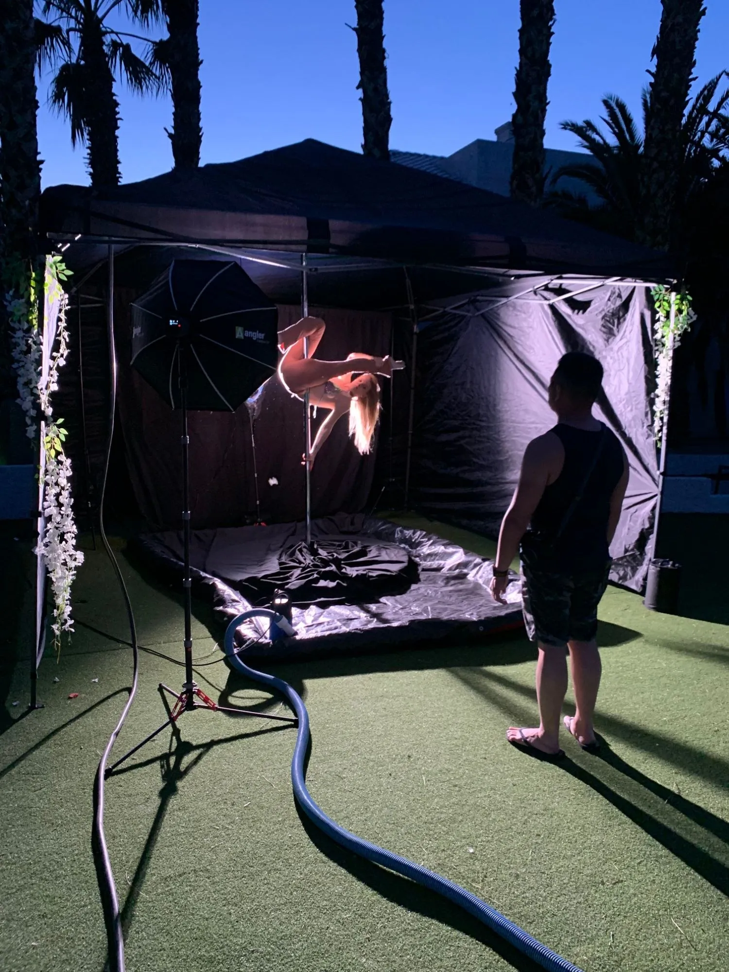 Dancer inverted on a rented pole under a lit canopy at an outdoor photo shoot